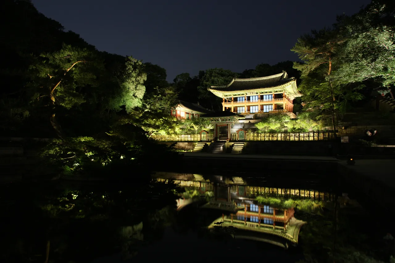 A lit Korean palace pavilion reflected in a still garden pond at night