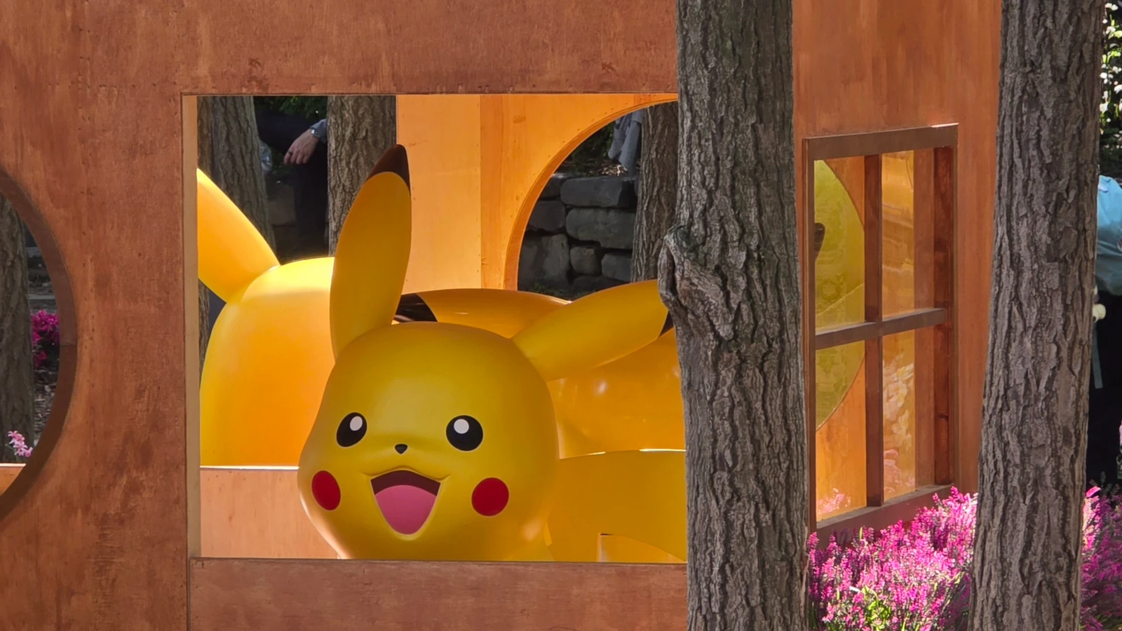 Large Pikachu figure looking out a wooden window at a forest Pokémon installation