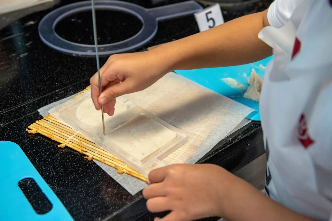Hands pressing fish paste into a mold on a tray during a hands-on fish cake making activity