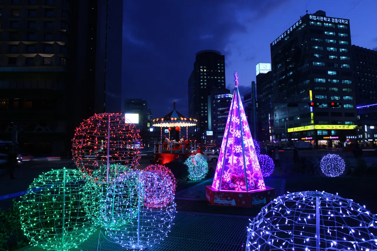 Seoul Plaza at night with glowing light spheres, a decorated tree, and a carousel, with office buildings behind