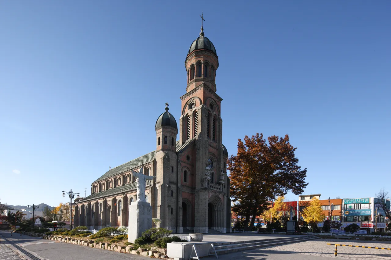 The brick Romanesque Jeondong Catholic Church under a clear sky with autumn trees, Jeonju