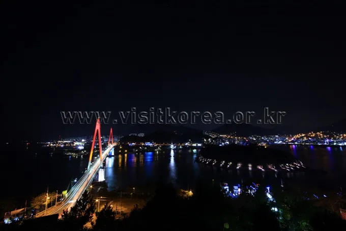 Dolsan Bridge lit at night over Yeosu harbor with city lights beyond