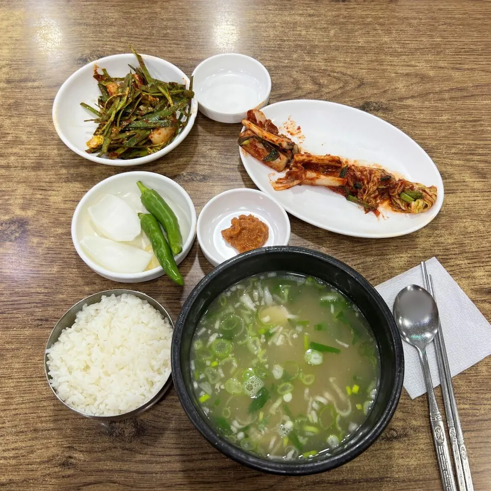 Overhead view of pork soup in a stone bowl with rice, kimchi, seasoned chives, onion and chili peppers