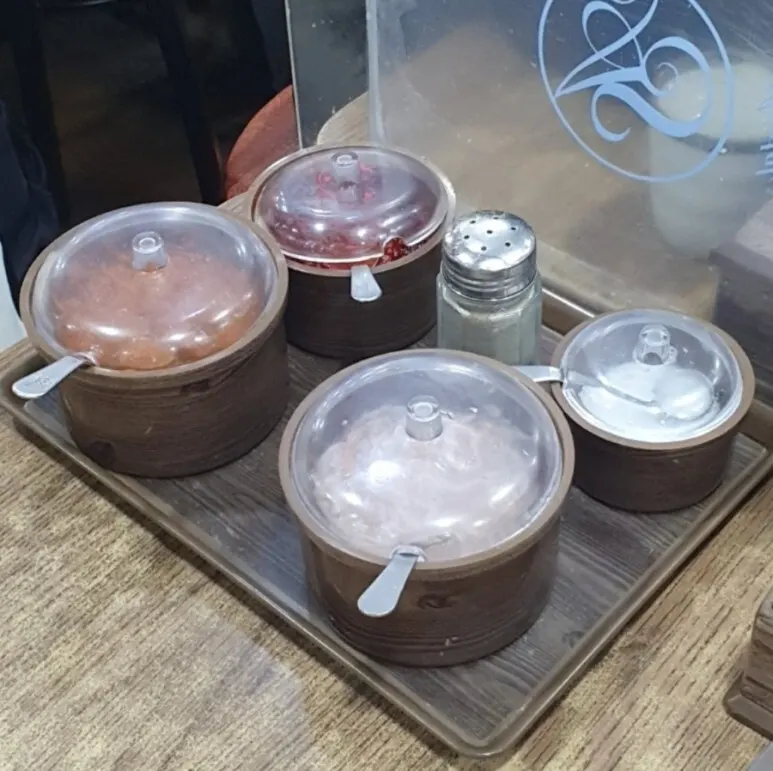 A tray of four lidded seasoning pots and a shaker on a wooden table