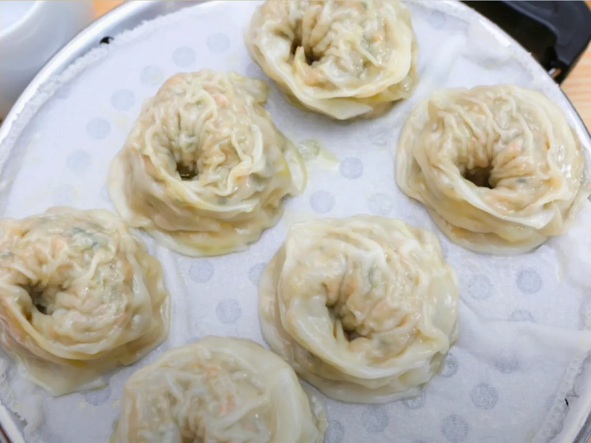 Six steamed dumplings on a cloth-lined steamer tray
