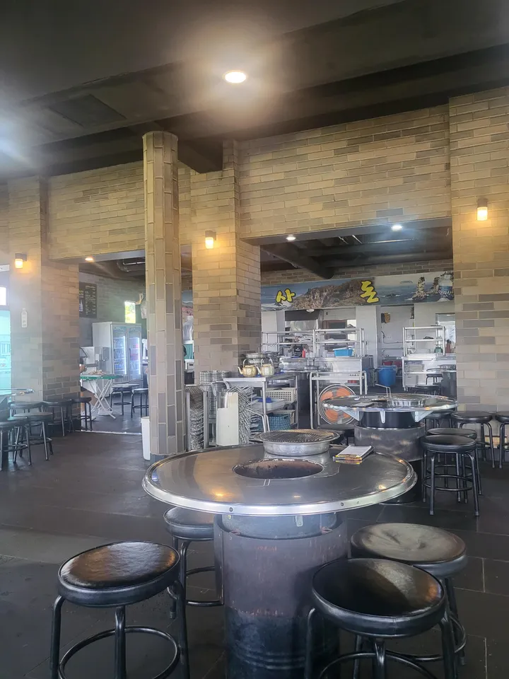 Open dining hall with round tables that have a central grill opening, black stools and a brick-pillared interior