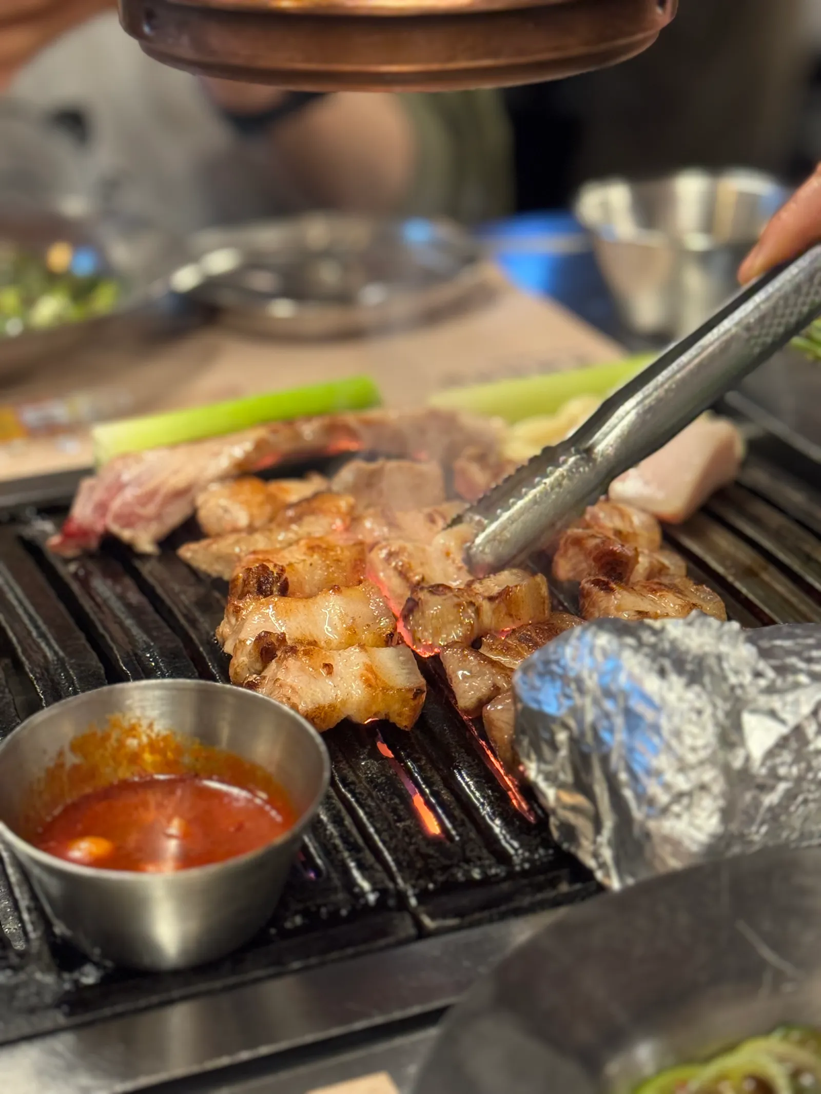 Thick-cut pork grilling over charcoal at Geumdwaeji Sikdang, with tongs and a dipping sauce beside the grill