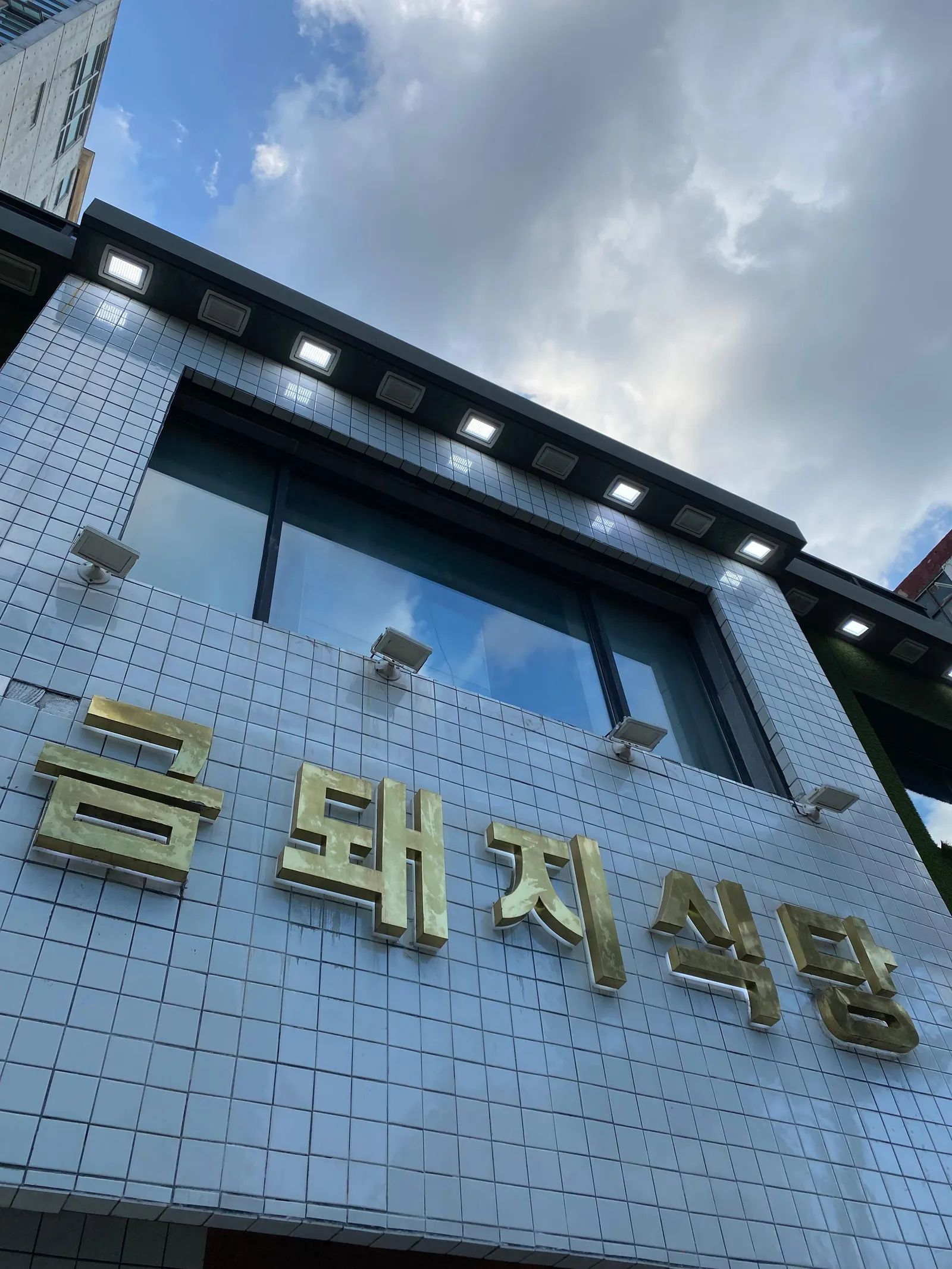 The gold Geumdwaeji Sikdang lettering on the white tiled frontage in Sindang