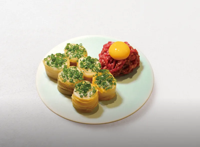 A celadon plate at Nanpo holding rolled parcels topped with spring onion and a mound of raw beef with an egg yolk